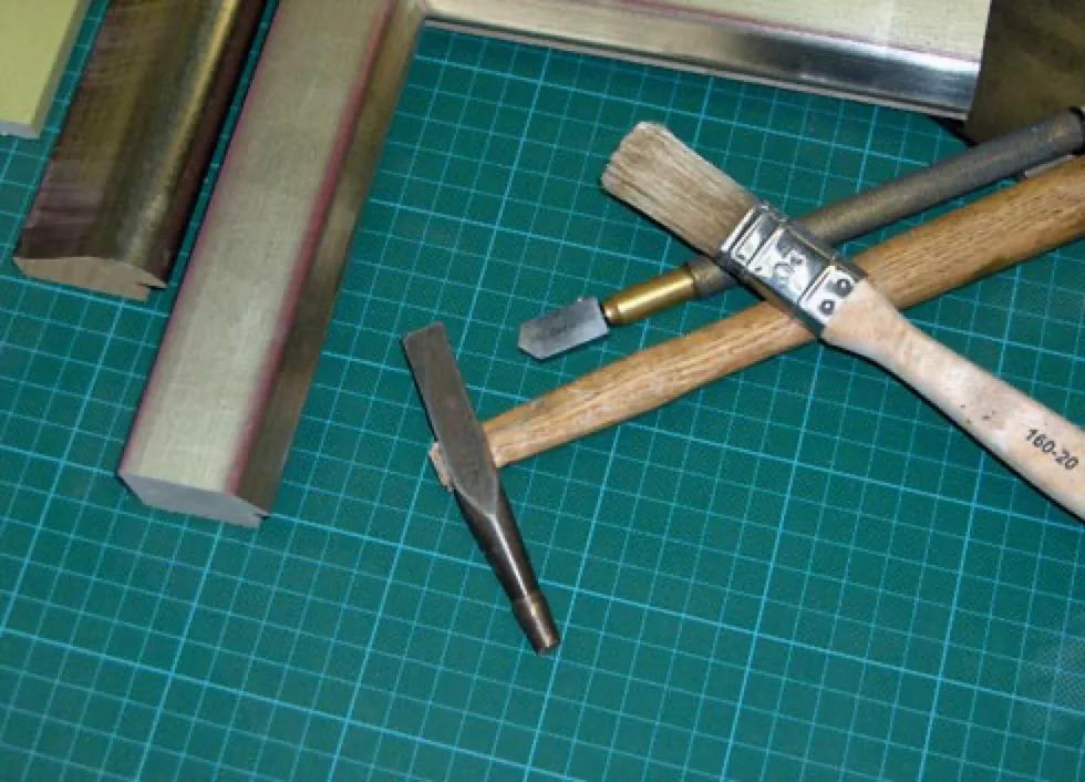 Goldleisten, Glasschneider, Hammer und Pinsel auf einer Schneidematte